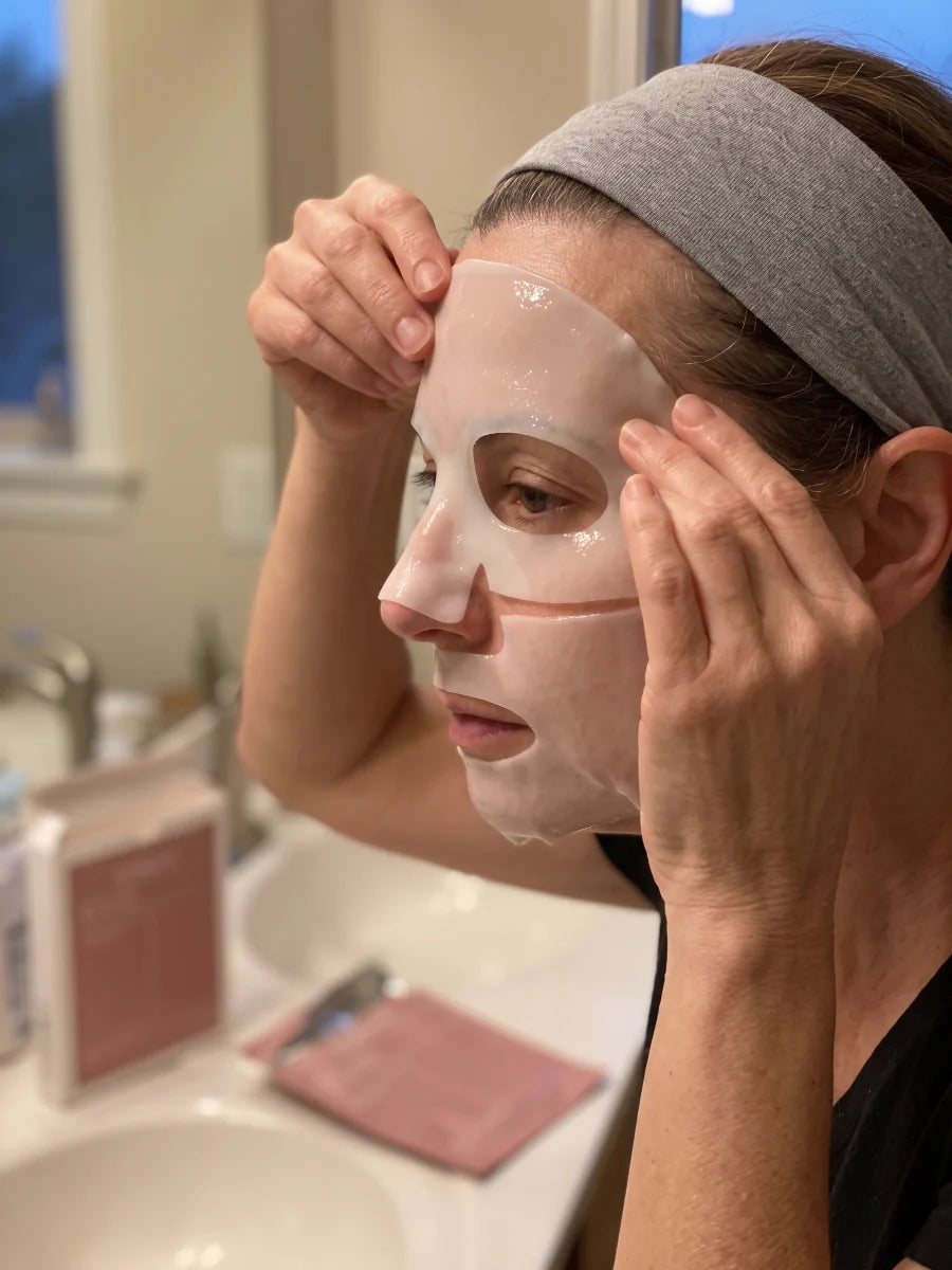 Mujer con una cinta en el pelo colocándose la mascarilla de hidrogel frente al espejo del baño