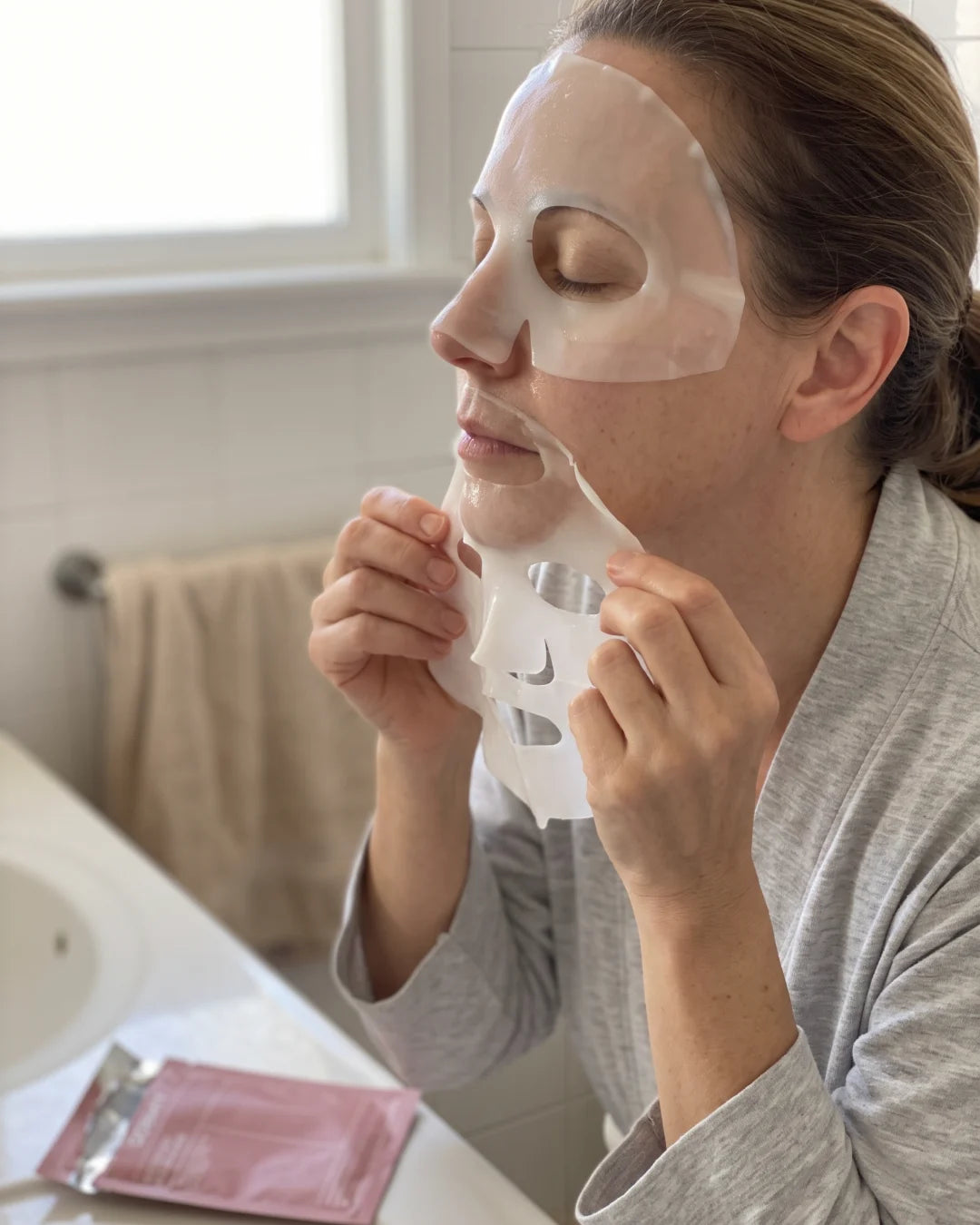 Por la mañana, una mujer con los ojos cerrados se quita despacio la parte de abajo de la mascarilla de hidrogel